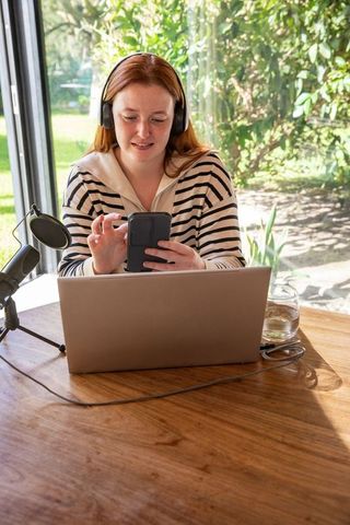 Young Woman Using Smartphone and Laptop with Headphones at Home Desk