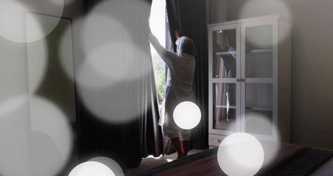 Senior woman pulling curtains revealing morning light in calm minimalist bedroom interior