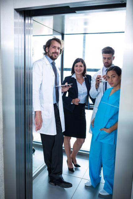 Doctors and a businesswoman are standing in an elevator in a hospital. The doctors are wearing medical uniforms, while the businesswoman is dressed in business attire. This image can be used to depict teamwork and collaboration in a healthcare setting, illustrating the intersection of medical and administrative roles in a hospital environment.