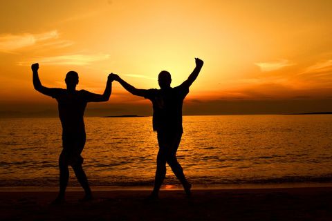 Joyful Silhouette of Friends Dancing on Seashore at Sunset