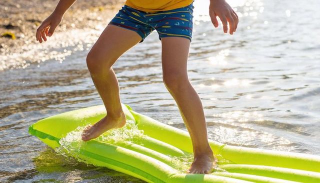 Child balancing on lime inflatable float in shallow water at sunny shoreline