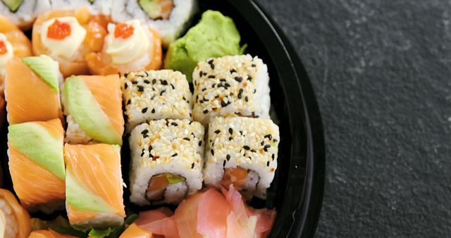 A variety of sushi rolls with different fillings and toppings are presented in a black dish, with copy space. Sushi is a traditional Japanese dish that has gained worldwide popularity for its unique flavors and artistic presentation.