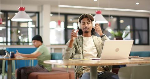 Young african american man adjusting headphones while working on laptop in coworking space