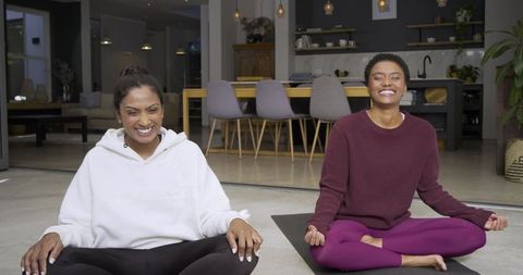 Diverse friends practicing yoga in open-plan kitchen wearing hoodies and vibrant leggings