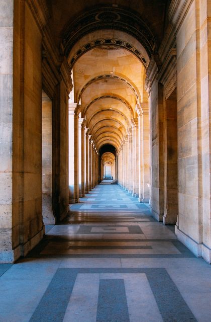 A long stone corridor features closely spaced arches and symmetrical design, illuminated by sunlight casting dramatic shadows across the floor. Useful for themes around historical architecture, cultural heritage, symmetry in design, or travel inspiration. Can be used in travel magazines, cultural blogs, and educational materials exploring historical sites.