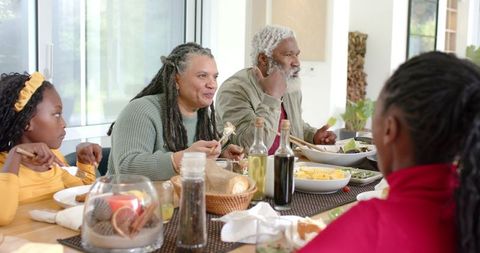 Multigenerational Diverse Family Sharing Casual Home Dinner Passing Bread and Conversing