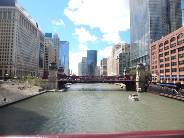 The image captures a picturesque view of Chicago River framed by towering skyscrapers and a prominent bridge under a clear blue sky. This photo is ideal for use in travel blogs, promotional materials for Chicago tourism, architectural reviews, and urban planning presentations.