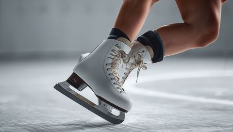 Figure skating closeup showing white leather skates and blades executing agile turn
