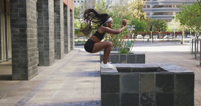 African american woman exercising outdoors wearing wireless earphones jumping in the city. healthy outdoor lifestyle fitness training.