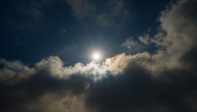 Sun illuminating clouds at dusk with crescent moon