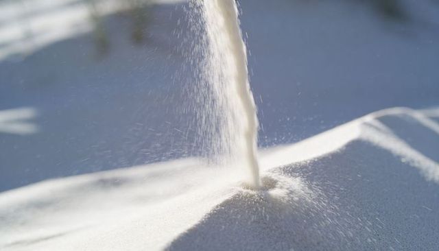 Pouring white sand forming conical mound with fine spray and soft shadows