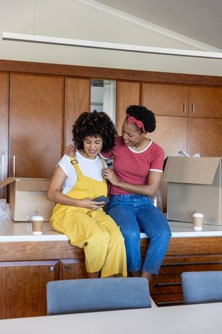 Diverse midadult women unpacking boxes and smiling on kitchen counter while moving home