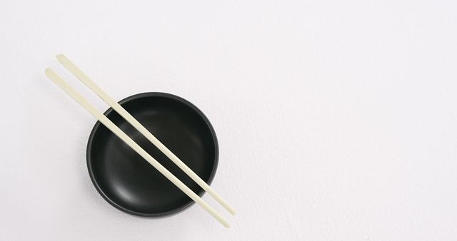 A pair of chopsticks rests on a black bowl against a white background, with copy space. The simplicity of the arrangement suggests a minimalist or Asian-inspired theme.