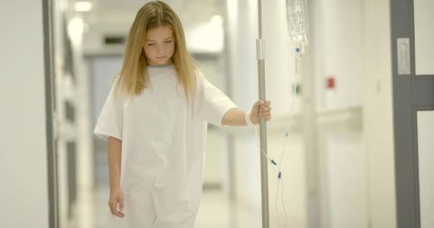 Young girl walking with IV pole in hospital corridor wearing patient gown