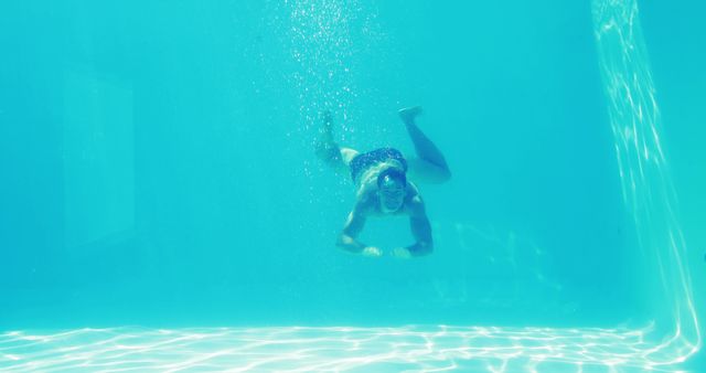 Image depicts a man swimming underwater in a clear blue pool. Ideal for use in advertisements for fitness programs, swimming lessons, vacation destinations, or aquatic-themed products. Suitable for illustrating relaxation and recreational activities.