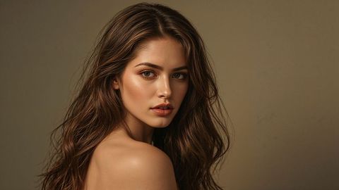 Elegant portrait of beautiful lady model with wavy brown hair on beige background