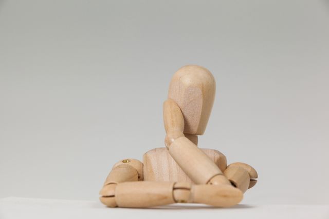 Wooden figurine leaning on table in a thoughtful pose against a white background. Ideal for illustrating concepts of creativity, contemplation, simplicity, and minimalism. Useful for art projects, educational materials, and creative design inspiration.