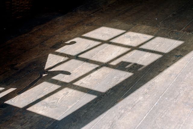 Sunlight casts through an old wooden window, forming patterns on a rustic wooden floor. It evokes feelings of peace, calm, and nostalgia. This timeless and minimalist image is perfect for use in home decor, interior design articles, or as a background in inspirational or reflective content.