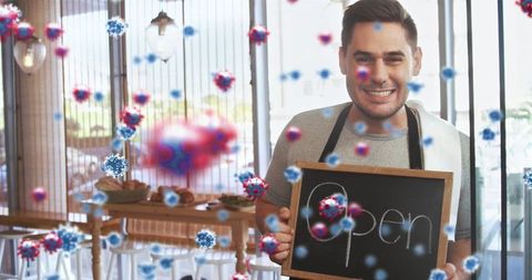 Barista Holding Open Sign with Overlaid Virus Particles and Cafe Background