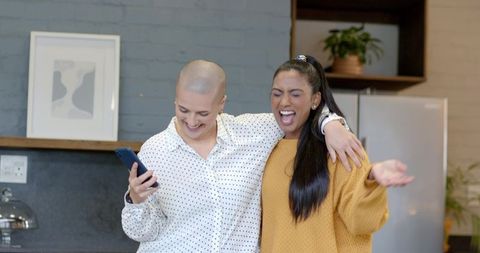 Laughing friends sharing smartphone moment in modern kitchen, warm candid togetherness