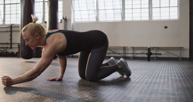 Female athlete stretching indoors on gym floor, focusing on fitness. Suitable for themes of health, fitness, exercising, training routines, workout programs, and athletic motivation.