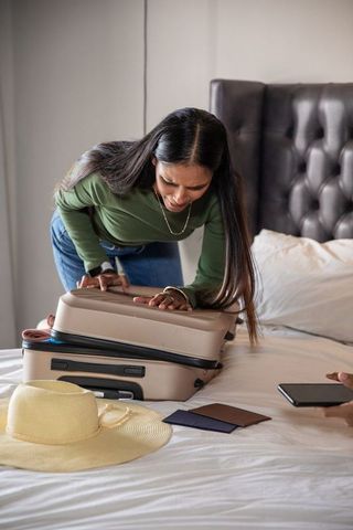 Woman Packing Suitcase Before Trip In Cozy Bedroom