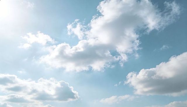 Sunlit cumulus clouds floating across pale blue sky with soft rim light and open space