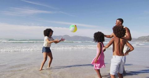 Family enjoying beach ball game by seaside on sunny day