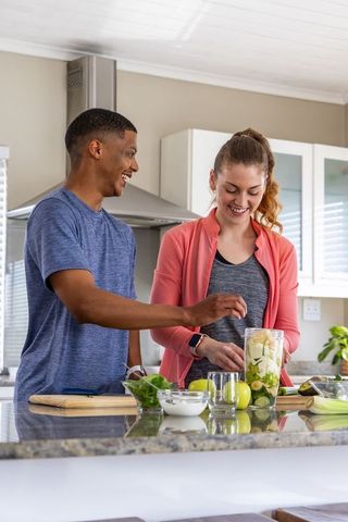 Diverse couple preparing green smoothie at modern kitchen island for healthy lifestyle