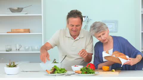 Senior Couple Joyfully Preparing Fresh Salad in Modern Kitchen