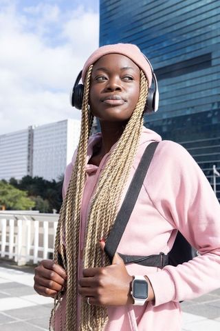 African american woman listening to music on city commute wearing pink hoodie and headphones