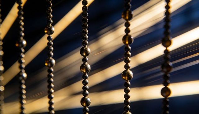 Hanging metallic bead chains catching warm diagonal light with golden reflections and blue bokeh