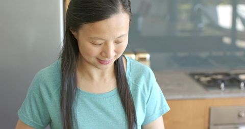 Smiling asian woman preparing meal while looking down in modern minimalist kitchen
