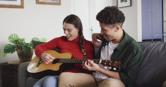 Happy biracial couple sitting on sofa in living room playing guitar - Download Free Stock Photos Pikwizard.com