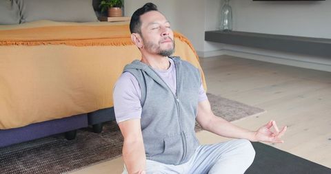 Mature Asian Man Practicing Meditation in Cozy Bedroom