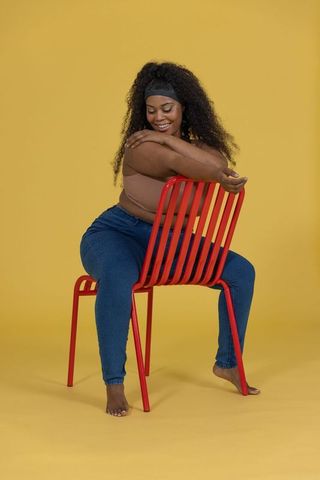 Confident african american woman sitting backward on red chair against mustard yellow