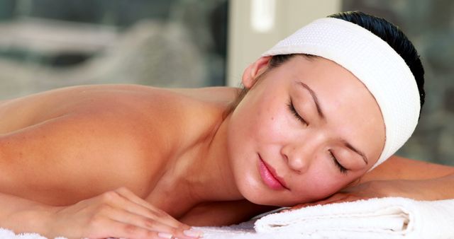 Woman lying down on comfortable surface at spa with headband on head, resting and appearing peaceful. Ideal for use in spa advertisements, wellness blog posts, beauty treatment promotions, relaxation-focused marketing materials, and self-care themed brochures.