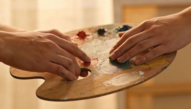 Artists mixing paint on wooden palette with paint-smeared fingertips, collaborative studio hands
