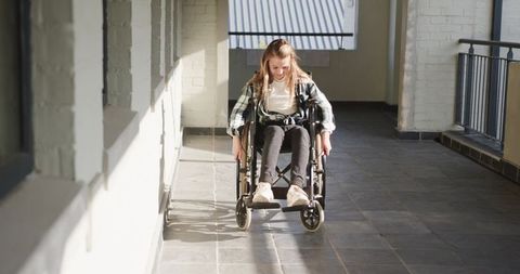 Young girl navigating sunlit corridor in wheelchair