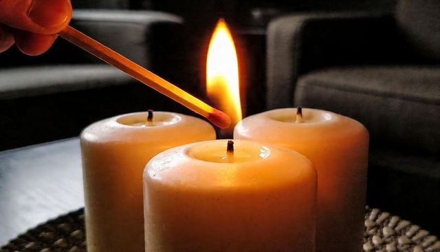 Hand Lighting Three Ivory Pillar Candles with Wooden Match Creating Cozy Ambient Glow