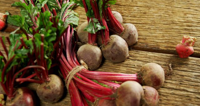 Fresh beetroots with vibrant green leaves and deep red stems are displayed on a rustic wooden surface, showcasing their natural, earthy state. Their rich colors and textures highlight the beetroots' freshness and readiness for culinary use.