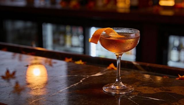 Coupe cocktail gleaming on marble bar with orange twist and scattered autumn leaves