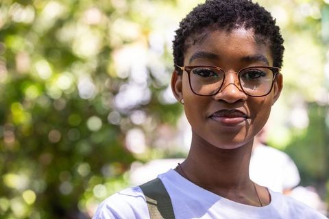 Young african woman wearing glasses and backpack in sunlit park lifestyle portrait bokeh