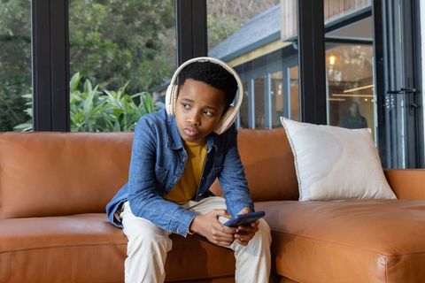 African american boy listening to music with headphones while holding smartphone