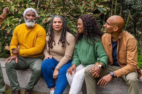 Multigenerational african american friends sitting on log bench holding hands in park