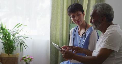 Senior Man with Doctor Discussing Health Using Tablet Technology in Care Facility
