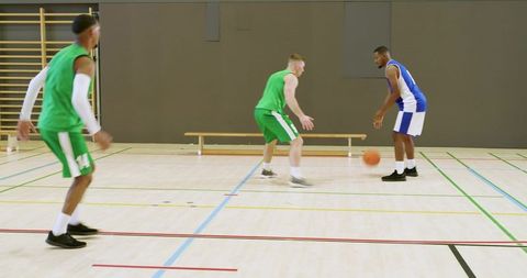 Blue guard performing between-legs dribble against green defenders on indoor court