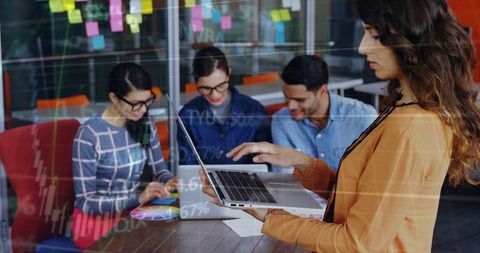 Woman presenting laptop while team collaborating with sticky notes and data charts