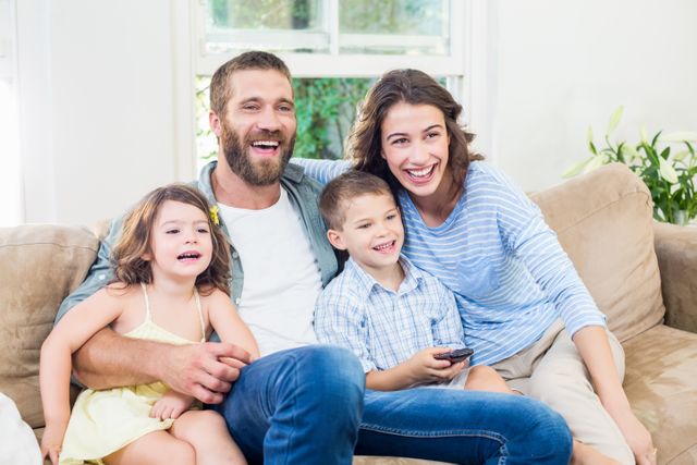 Family sitting on sofa enjoying television together. Perfect for use in advertisements, family-oriented content, lifestyle blogs, and articles about family bonding and home entertainment.