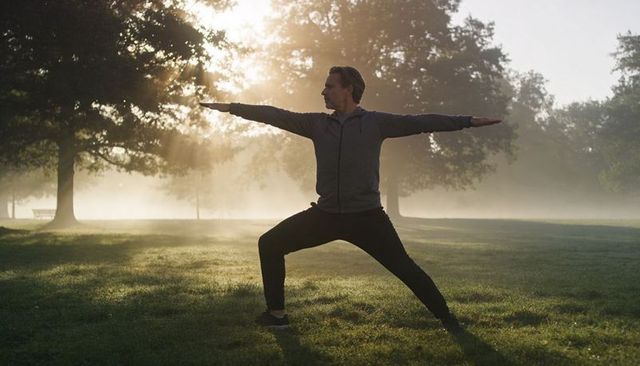 Man practicing warrior yoga pose at misty sunrise in park for mindfulness and fitness